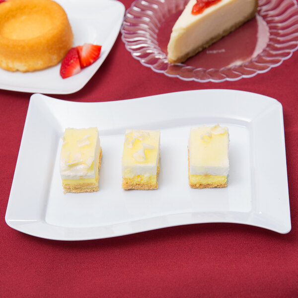 A Fineline white plastic dessert plate with a slice of cheesecake and strawberries on a red tablecloth.