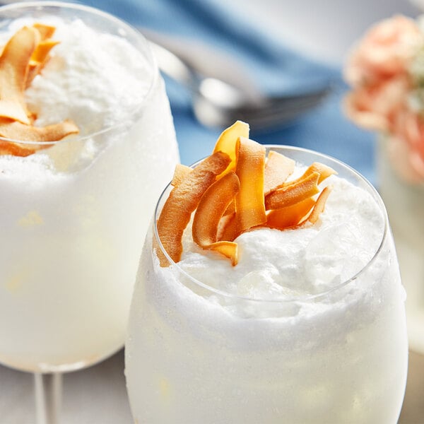 Two glasses of white coconut milk with whipped cream and orange peels on top.