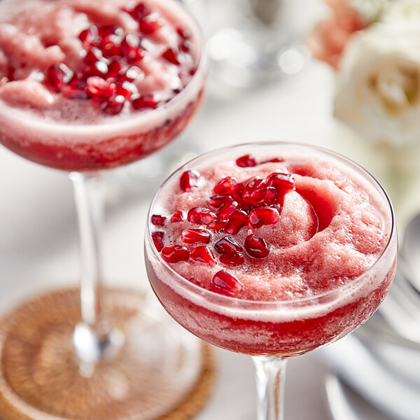 A glass of pink pomegranate and raspberry drink with pomegranate seeds.