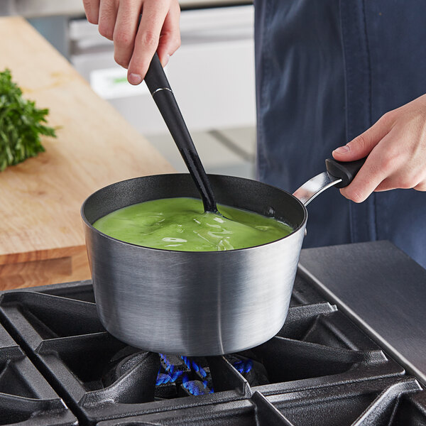 A person cooking green soup in a Vollrath Wear-Ever sauce pan on a stove.