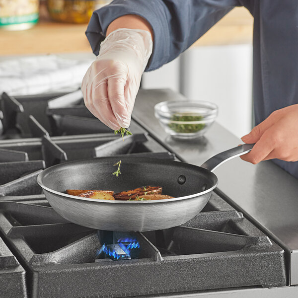 A person cooking food in a Vollrath Wear-Ever aluminum non-stick fry pan on a gas stove.