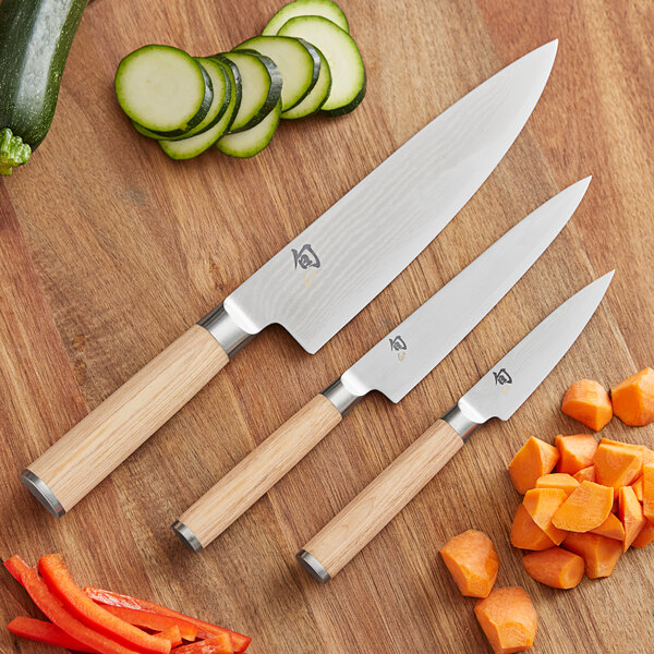 A Shun Classic knife set with wooden handles cutting carrots on a table.