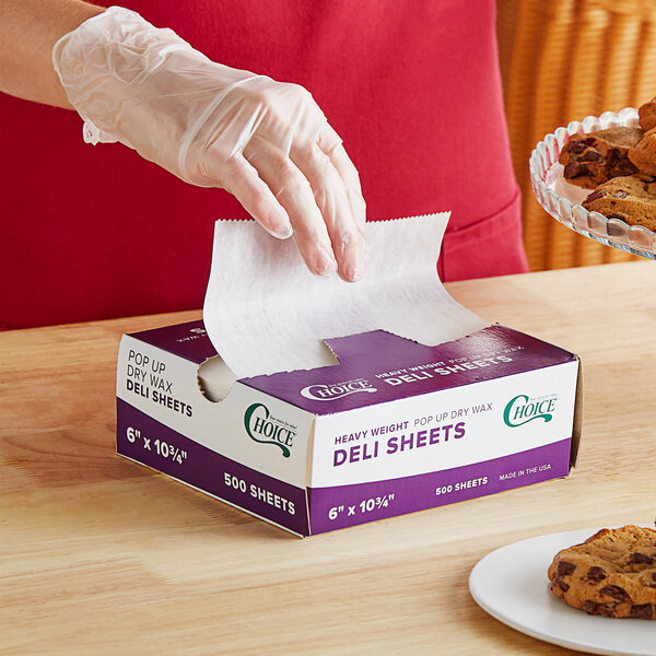 A person wearing a plastic glove using Choice Interfolded Deli Wrap to line a box of cookies.