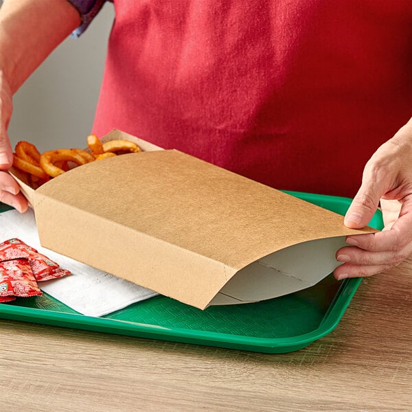 A person holding a box of fries in a Kraft paper food sleeve.