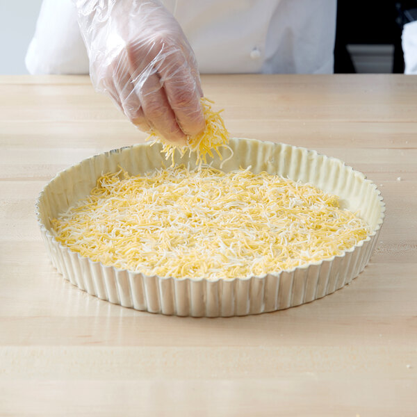 A person sprinkling cheese in a Gobel round fluted tart pan.
