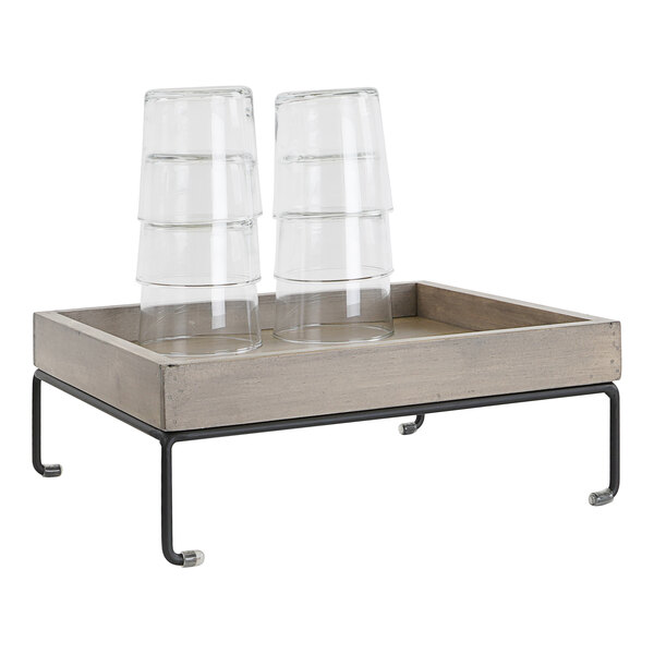 A wood display riser with a metal base holding clear plastic cups.