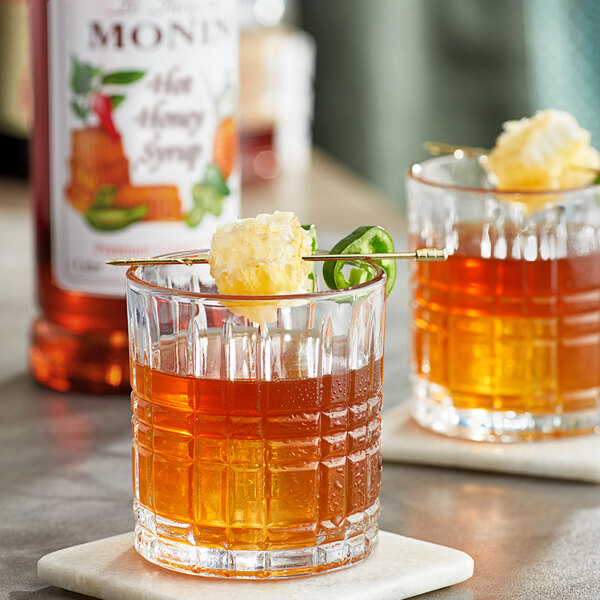 Two glasses of Monin Hot Honey whiskey garnished with a pineapple stick.
