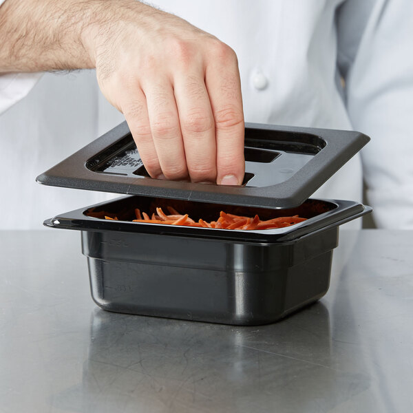 A hand using a black Cambro lid to open a container of food.