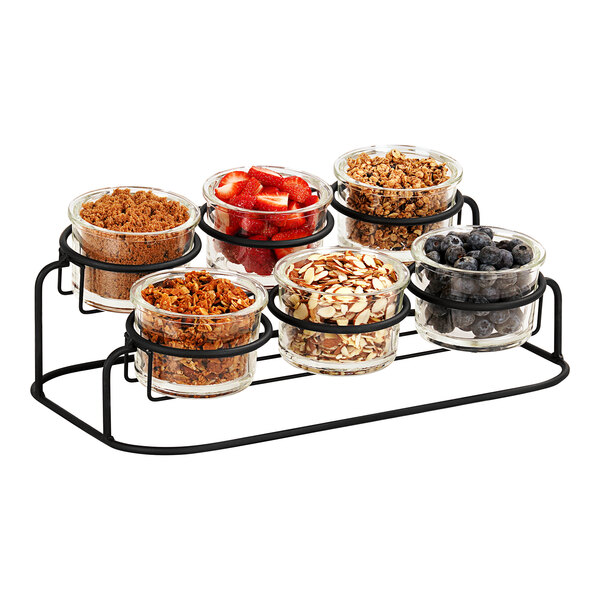 A Cal-Mil black 2-tier condiment display with glass containers of different foods.