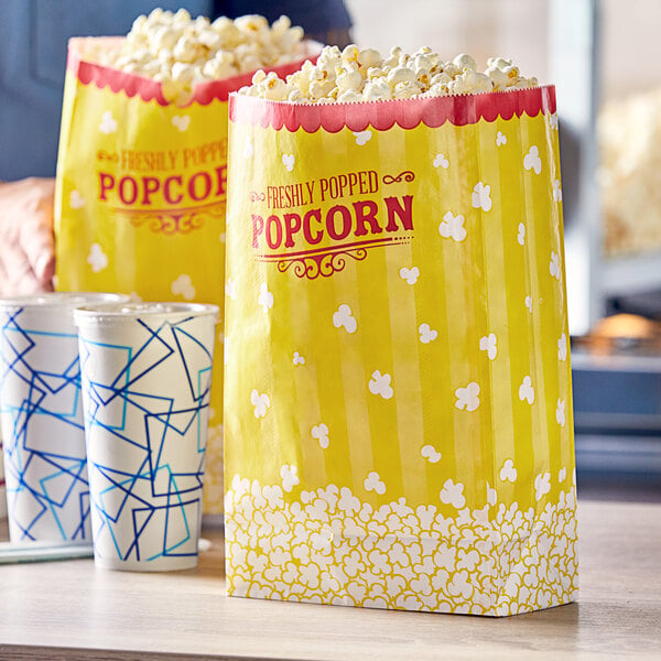 A yellow and white Carnival King popcorn bag on a table with two cups.