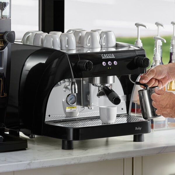 A person pouring coffee into a Gaggia espresso machine on a metal counter.