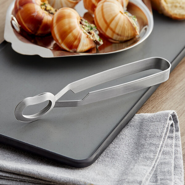 Stainless steel tongs serving a plate of snails.