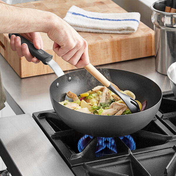 A person cooking food in a Vollrath SteelCoat stir fry pan on a stove.