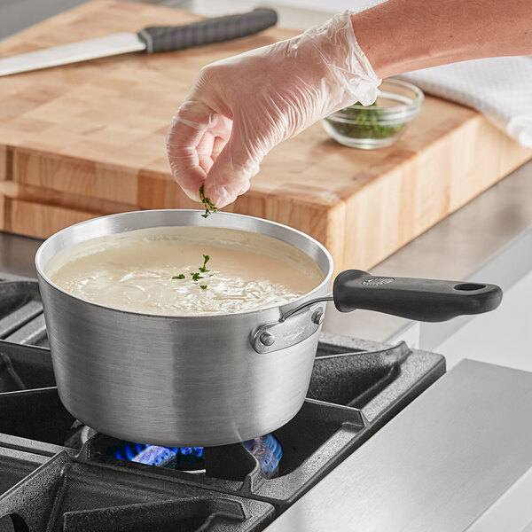 A hand using a Vollrath Wear-Ever sauce pan to cook soup on a stove.