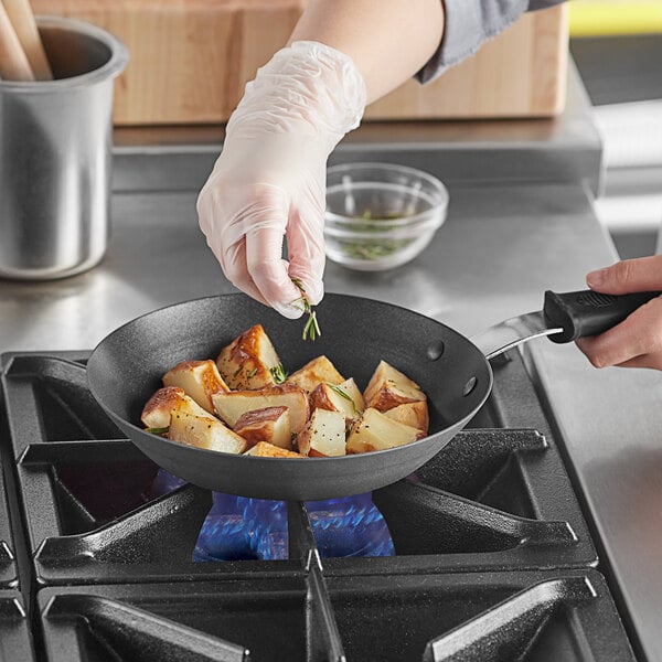 A person cooking potatoes and rosemary in a Vollrath carbon steel non-stick fry pan with a black silicone handle.