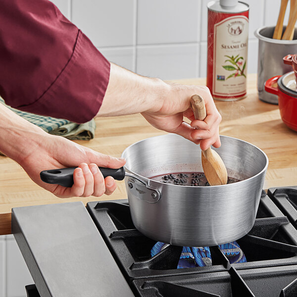 A person stirring food in a Vollrath Wear-Ever sauce pan on a stove.