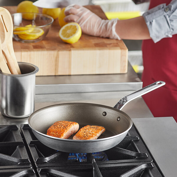 A person cooking two pieces of salmon in a Vollrath aluminum non-stick fry pan.