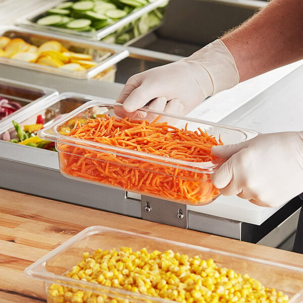 A person in gloves holding a Choice clear polycarbonate food pan filled with carrots.