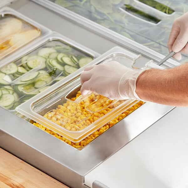 A person in gloves using a Choice clear plastic food pan lid with a notch and handle to cover a container of food on a salad bar counter.