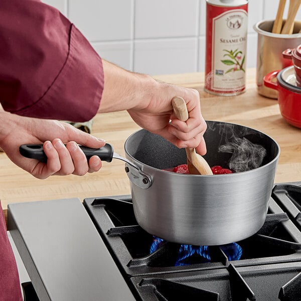 A person stirring food in a Vollrath Wear-Ever non-stick aluminum sauce pan with a black silicone handle.