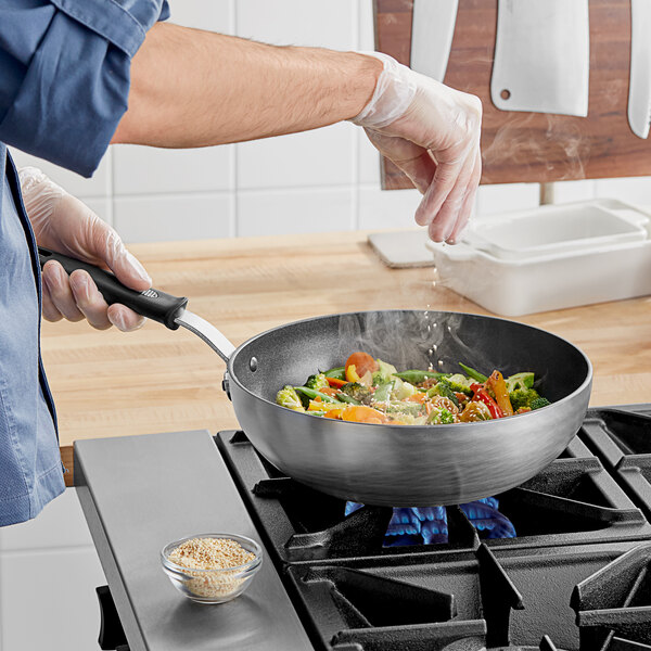 A person using a Vollrath SteelCoat Non-Stick Stir Fry Pan to cook food on a stove.