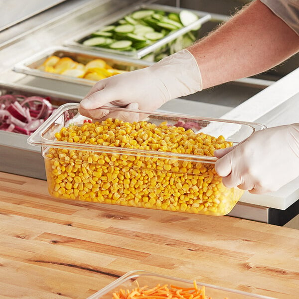 A person in gloves holding a Choice clear polycarbonate food pan filled with corn.