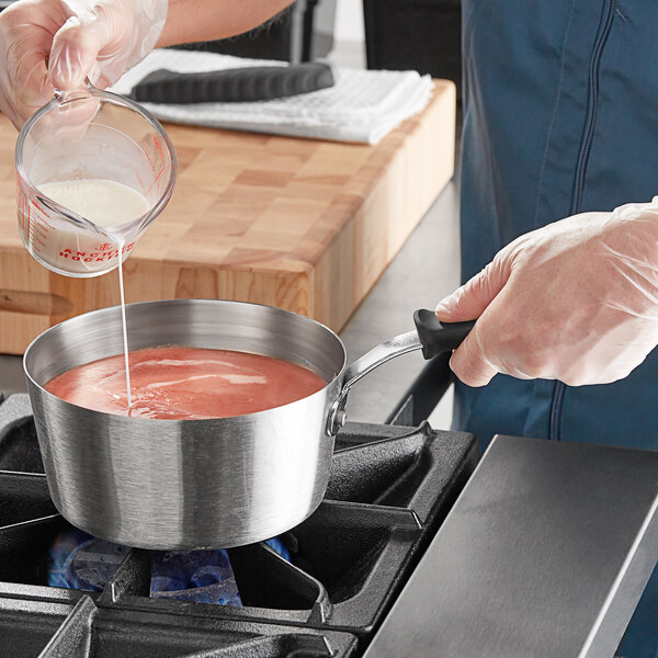 A person pouring liquid into a Vollrath stainless steel sauce pan on a stove.