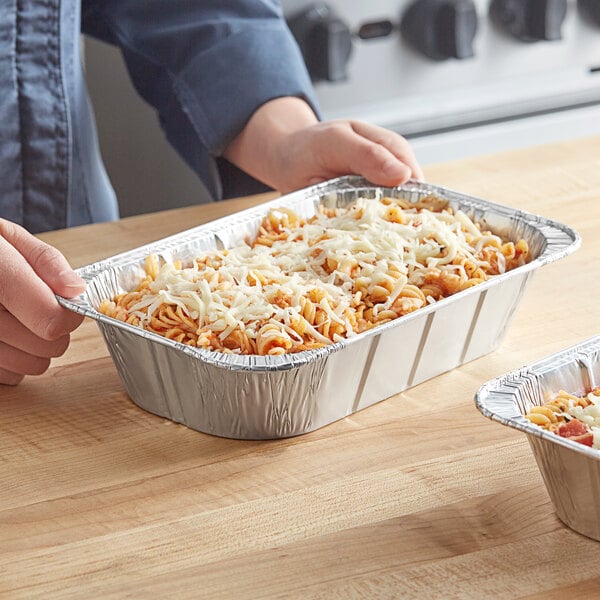 A person holding a Western Plastics foil steam table pan of pasta with cheese.