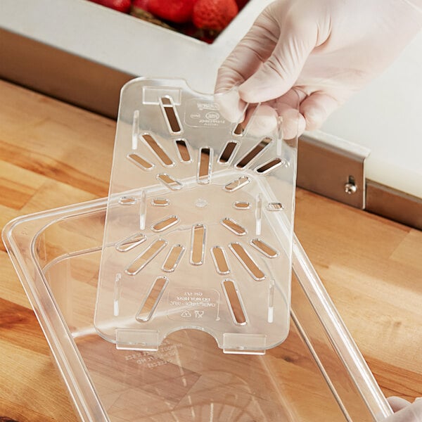 A hand holding a Choice clear polycarbonate drain tray with strawberries.