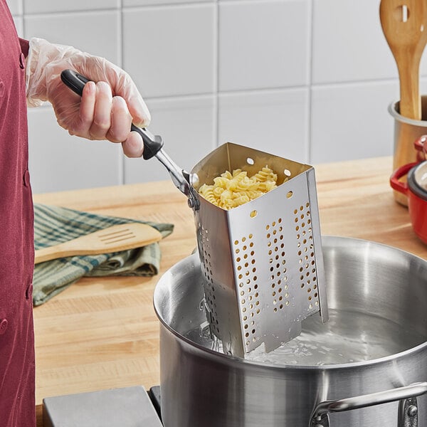 A person using a Vollrath stainless steel pasta basket to cook pasta in a pot.