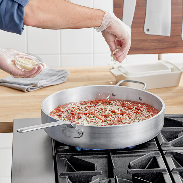 A person cooking pasta in a Vollrath Wear-Ever saute pan.