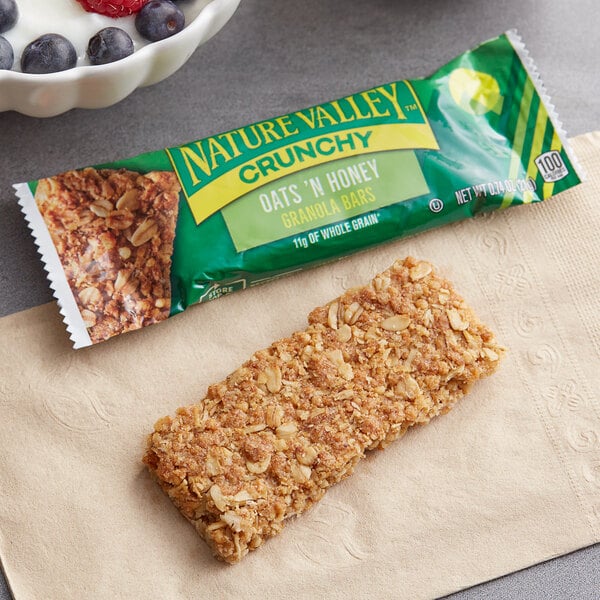 A Nature Valley Oats and Honey Crunchy Granola Bar on a napkin next to a bowl of fruit.