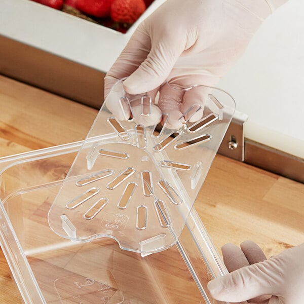 A person in gloves holding a Choice clear polycarbonate drain tray on a counter in a salad bar.