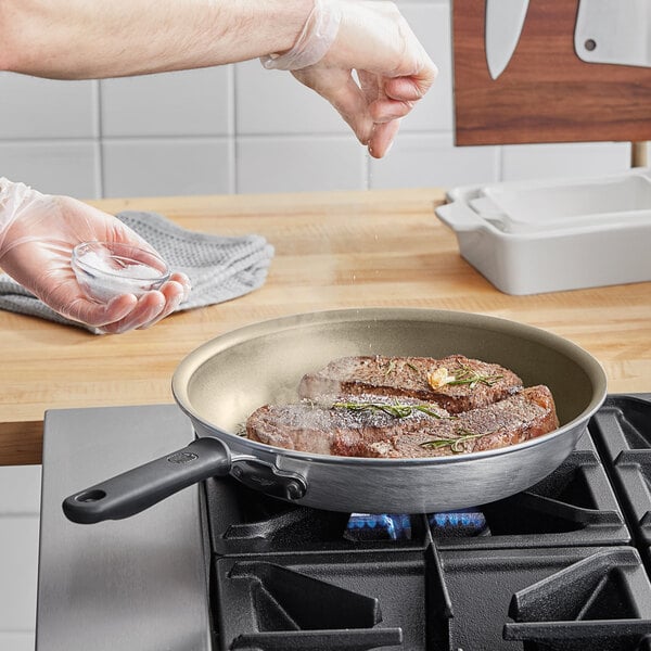 A person cooking a steak in a Vollrath Wear-Ever non-stick fry pan on a stove.