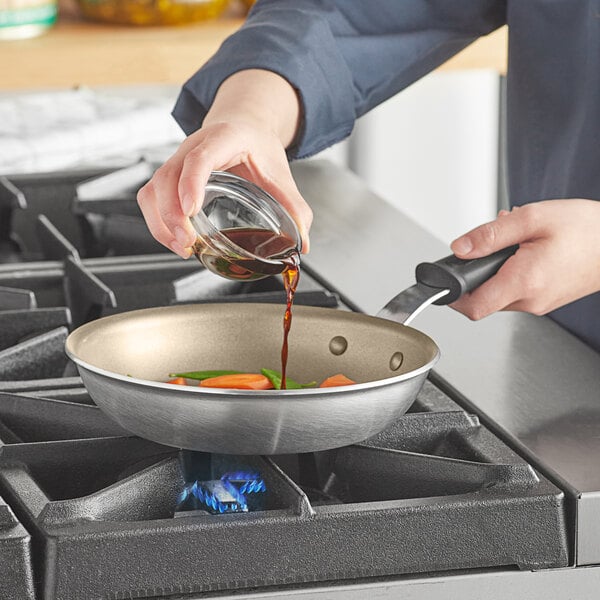A person pouring brown sauce into a Vollrath Wear-Ever non-stick fry pan.