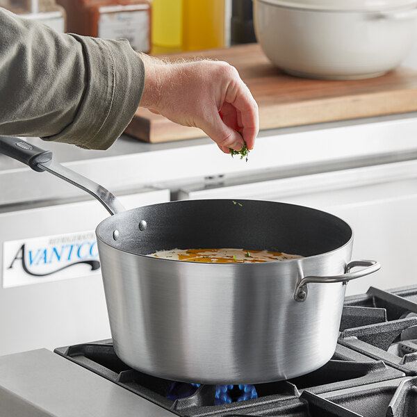A person stirring food in a Vollrath Wear-Ever sauce pan on a stove.