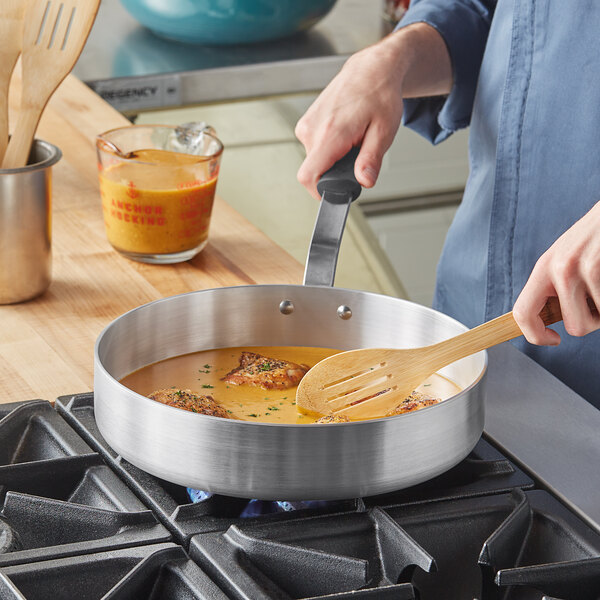 A person cooking food in a Vollrath aluminum saute pan.