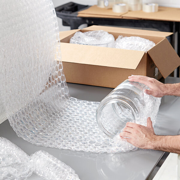 A man using Lavex Large Perforated Bubble Roll to pack a glass jar.