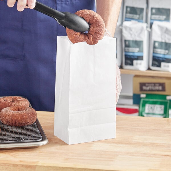 A man holding a donut in a Choice waxed paper bag on a bakery display counter.
