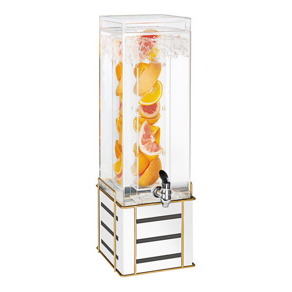 A Cal-Mil beverage dispenser with oranges and lemons in the infusion chamber on a white and gold metal base.