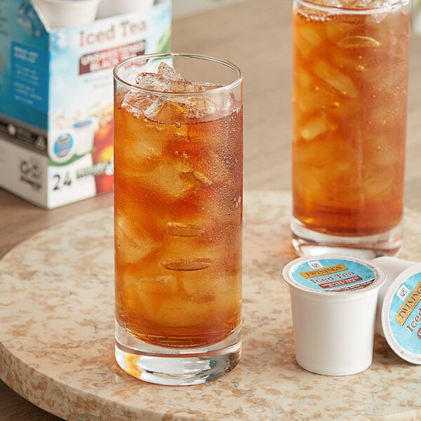 A glass of iced black tea with ice next to a box of Twinings K-Cup Pods.