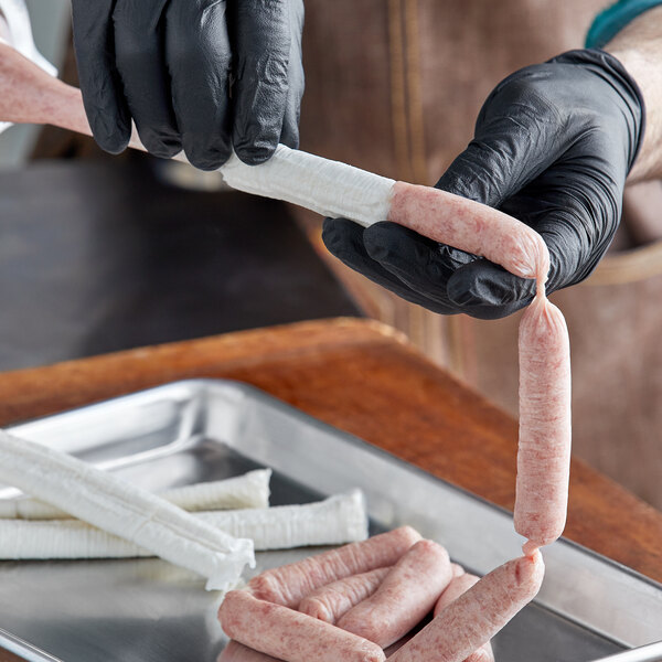 A person in black gloves is cutting a long sausage in a butcher shop.