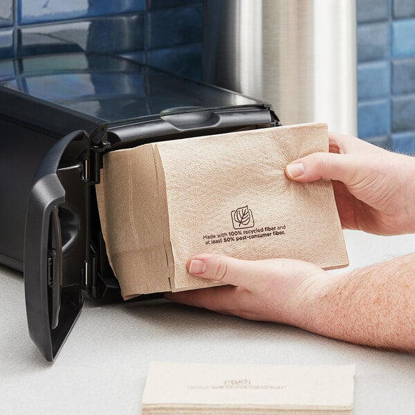 A hand holding a Dixie Ultra brown interfold paper napkin over a counter.