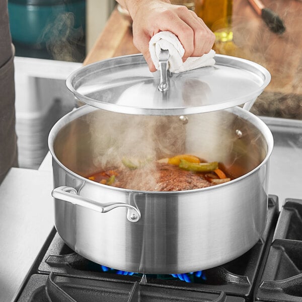 A person using a Vigor stainless steel brazier to cook food on a stove.