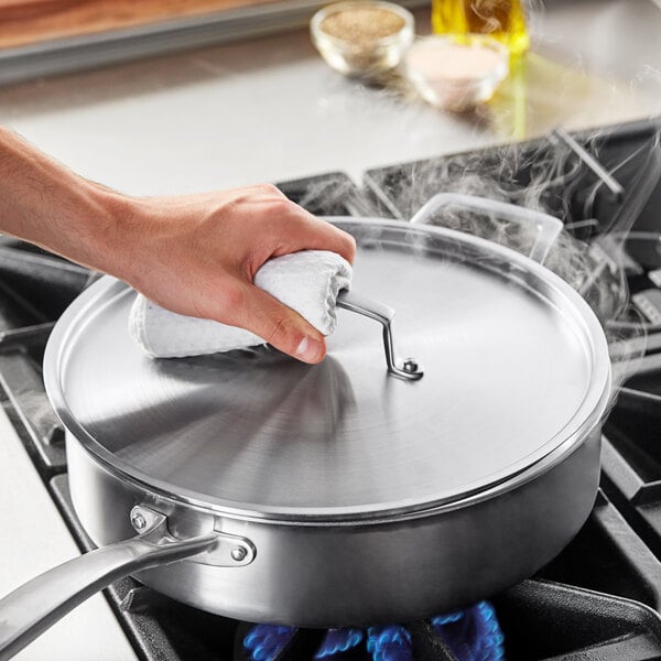 A hand using a white cloth to clean a stainless steel pan.