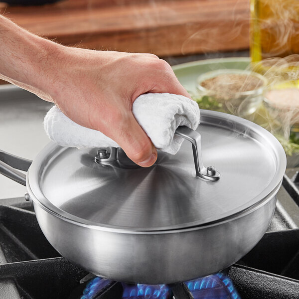 A person holding a Vigor stainless steel lid over a pan.