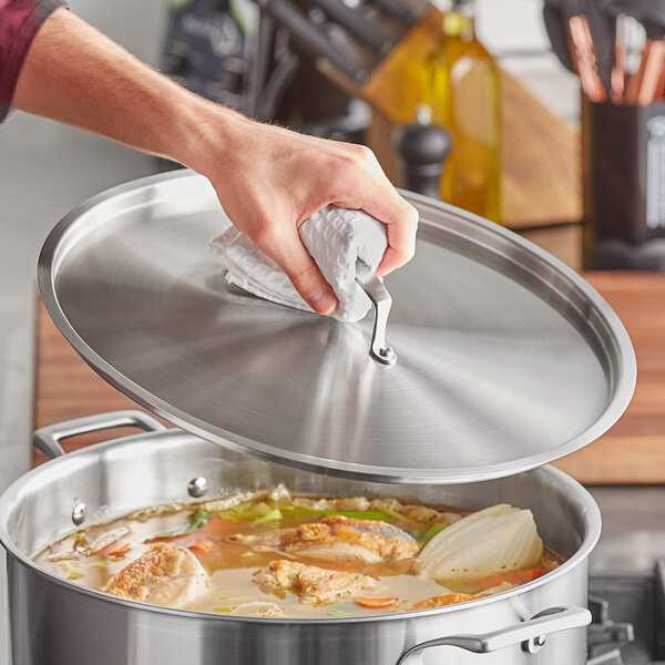 A hand using a white towel to clean a stainless steel lid on a pot.