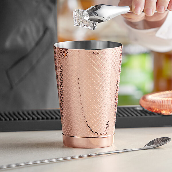 A bartender using a Barfly copper cocktail shaker to pour a drink.