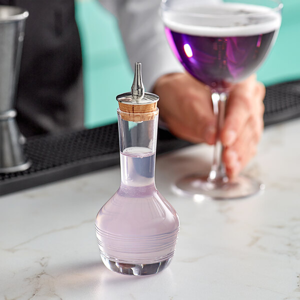 A person holding a Barfly glass bitters bottle filled with purple liquid.