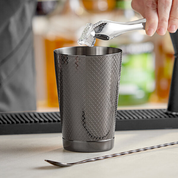 A person using a Barfly black and silver diamond lattice cocktail shaker to pour a drink.